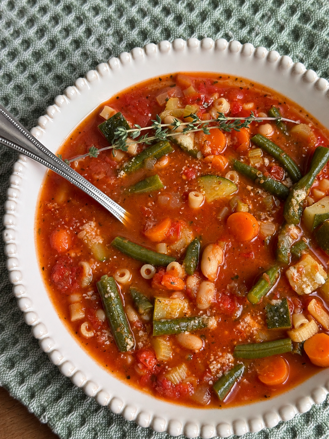 Spoon resting in a bowl of vegetable minestrone with white beans and small pasta
