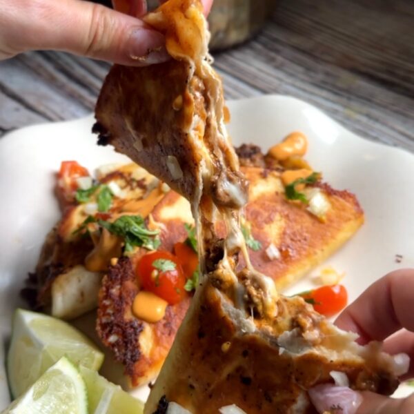 Crispy beef taco pulled apart to show melted cheese, topped with chipotle sauce, tomatoes and cilantro
