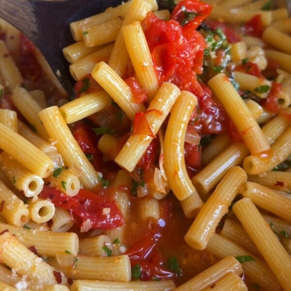 Rigatoni tossed with burst cherry tomatoes and herbs in a pan with a wooden spoon