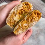 Hand holding a butter chicken burrito cut open to show rice and saucy chicken
