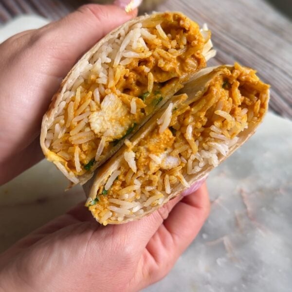 Hand holding a butter chicken burrito cut open to show rice and saucy chicken