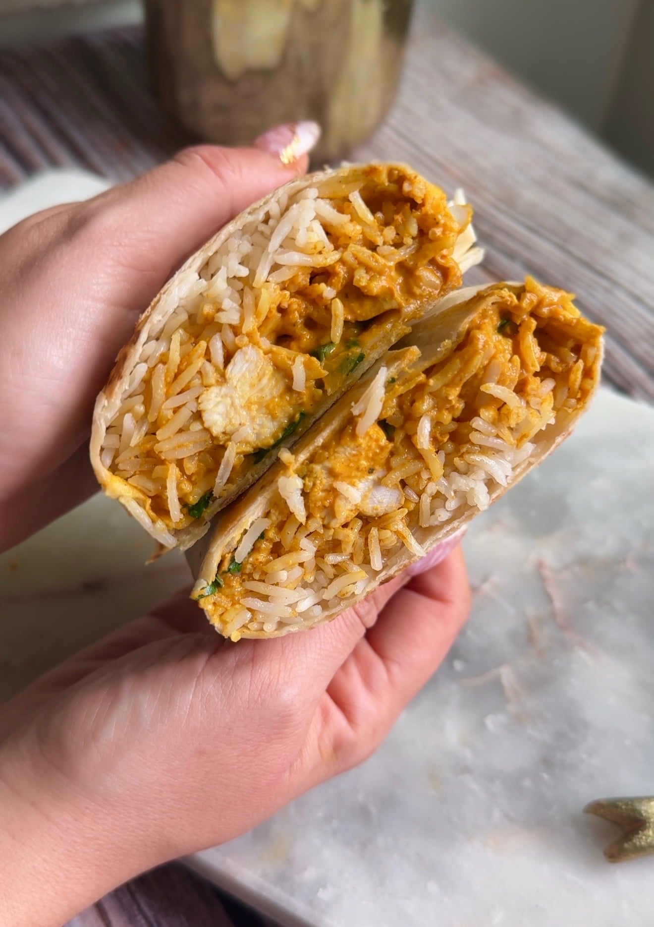 Hand holding a butter chicken burrito cut open to show rice and saucy chicken