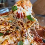 Cheesy stuffed shells lifted from the baking dish in a long cheese pull with basil