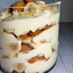 Layered banana pudding in a glass trifle dish with vanilla wafers, bananas and cream