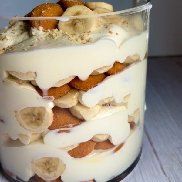 Layered banana pudding in a glass trifle dish with vanilla wafers, bananas and cream