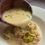 Creamy chicken and wild rice soup ladled into a white bowl with celery and carrots