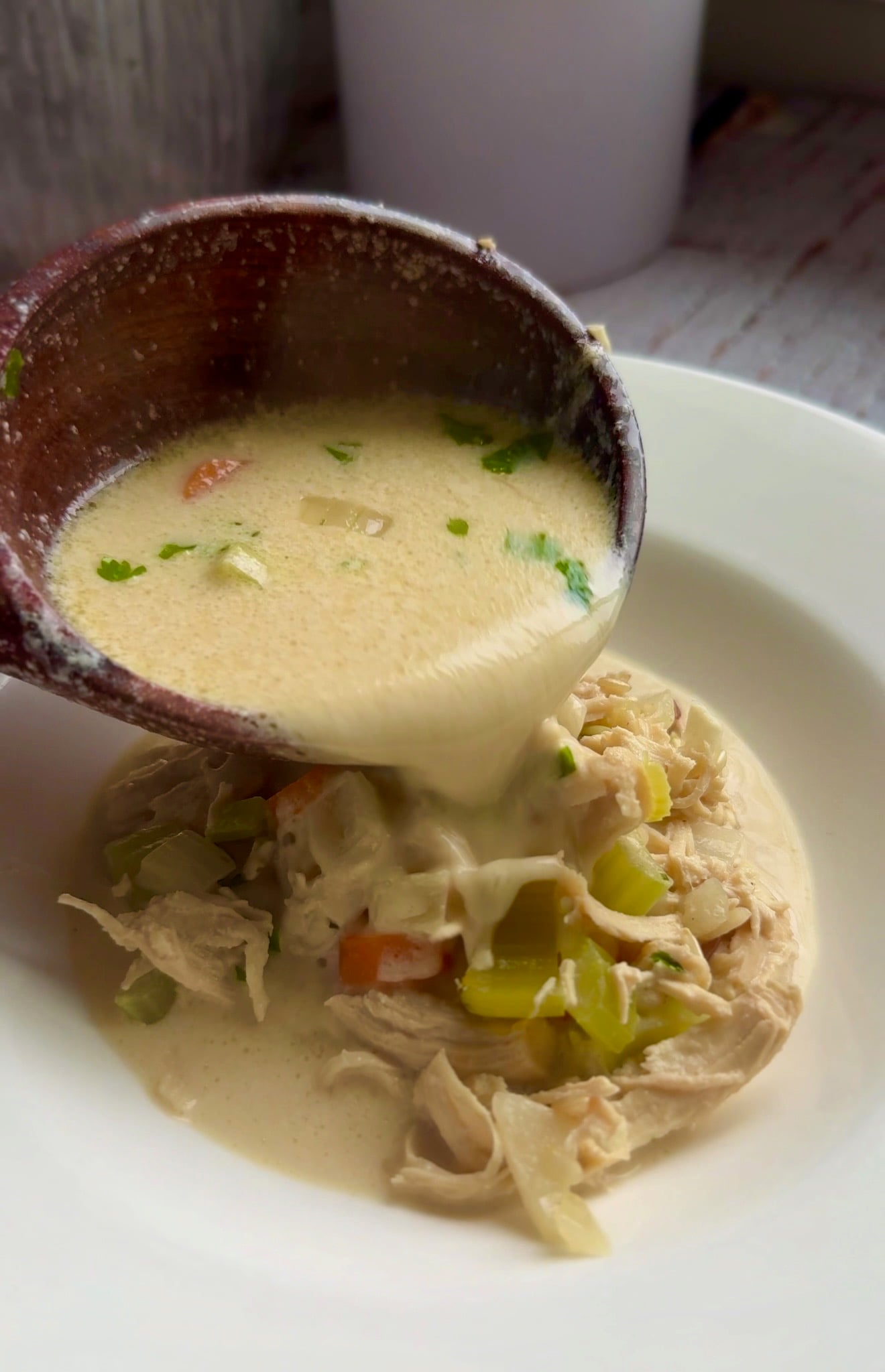 Creamy chicken and wild rice soup ladled into a white bowl with celery and carrots