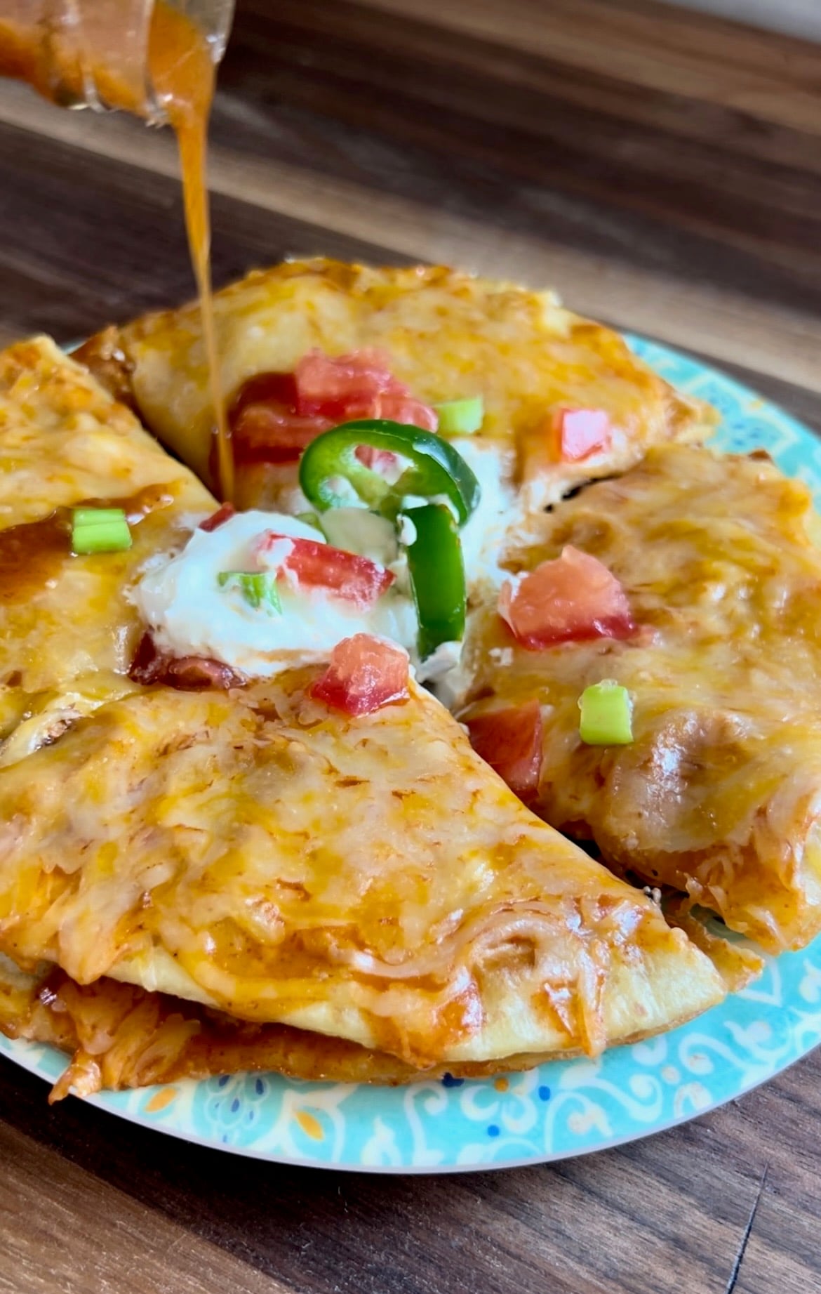 Copycat Mexican pizza on a turquoise plate with melted cheese, sour cream and jalapeno