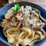 Fettuccine alfredo topped with sliced seared chicken and parsley in a blue bowl