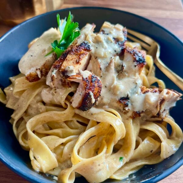 Fettuccine alfredo topped with sliced seared chicken and parsley in a blue bowl