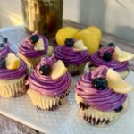 Lemon blueberry cupcakes swirled with purple frosting, topped with berries and lemon