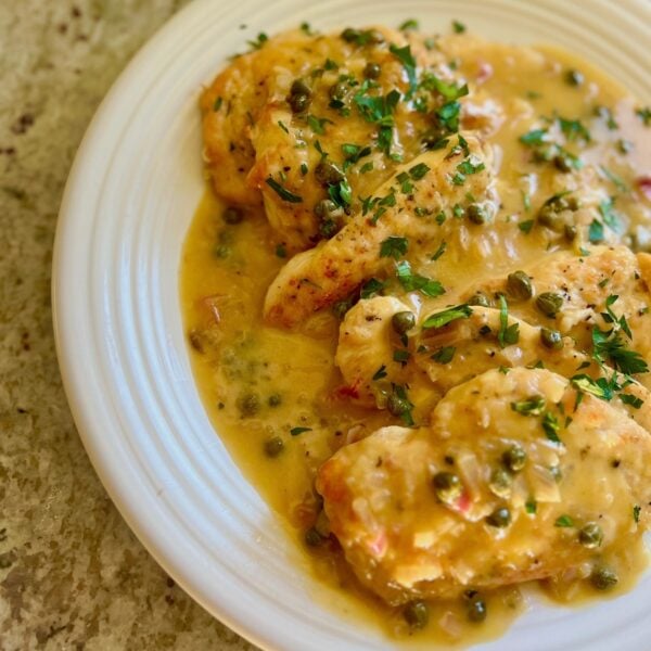Chicken piccata cutlets in a lemon caper sauce on a white plate with parsley