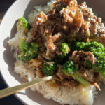 Beef and broccoli served over steamed rice in a white bowl with a gold fork