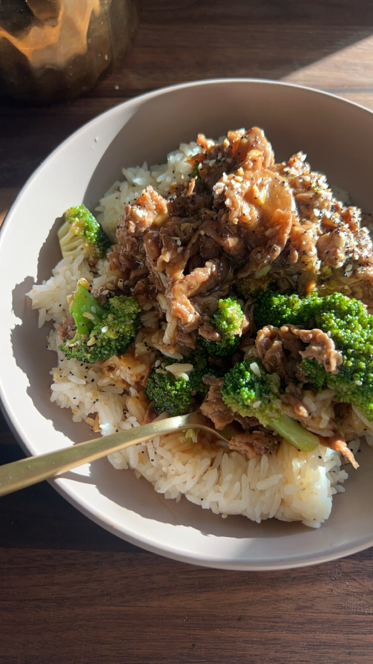 Beef and broccoli served over steamed rice in a white bowl with a gold fork