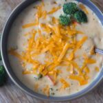 Creamy broccoli cheddar soup in a dark bowl, topped with shredded cheddar and broccoli