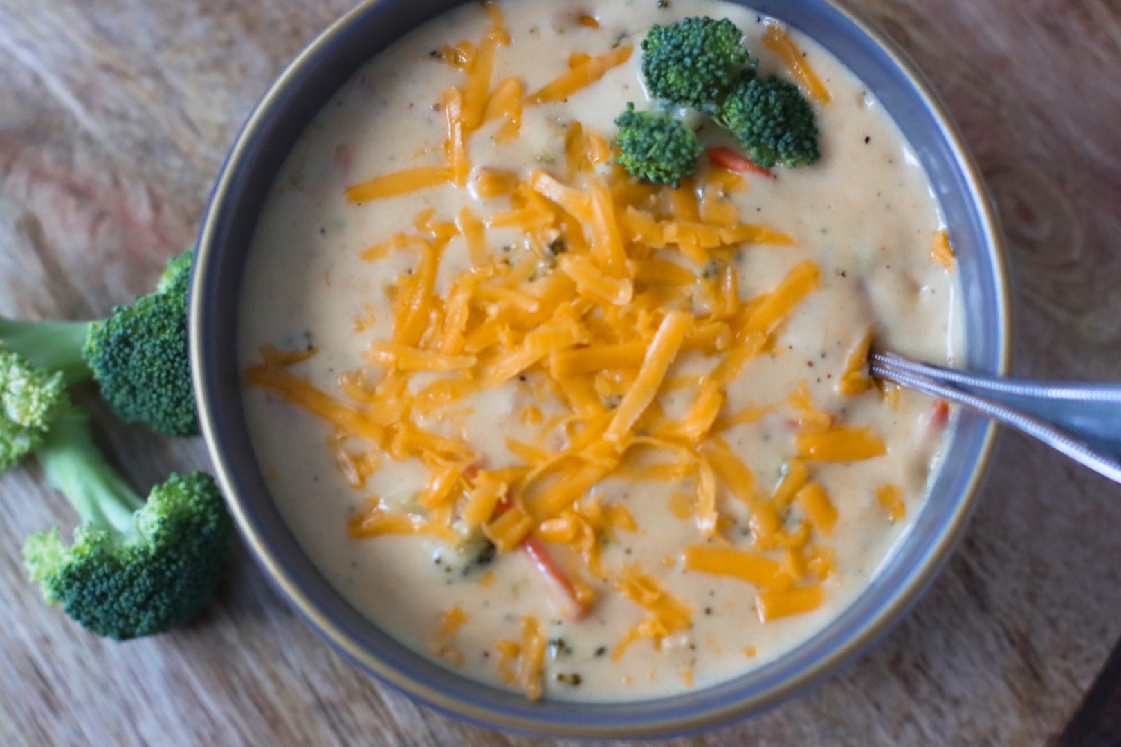 Creamy broccoli cheddar soup in a dark bowl, topped with shredded cheddar and broccoli
