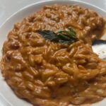 Creamy orzo alla vodka in a white bowl topped with fresh basil leaves