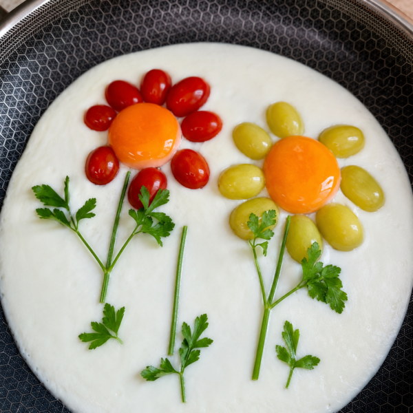 Over easy eggs in a skillet arranged as flowers with tomato petals and parsley stems