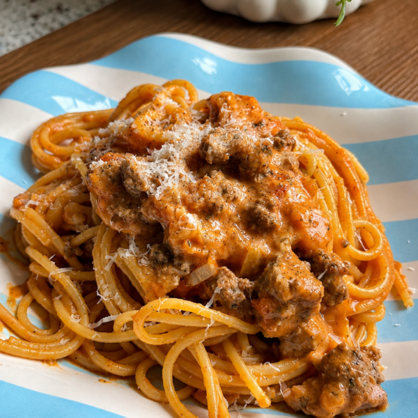 Spaghetti under chunky meat sauce and grated parmesan on a blue striped plate