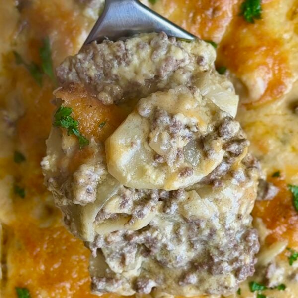 Server lifting beef and scalloped potatoes from a bubbling cheddar topped casserole