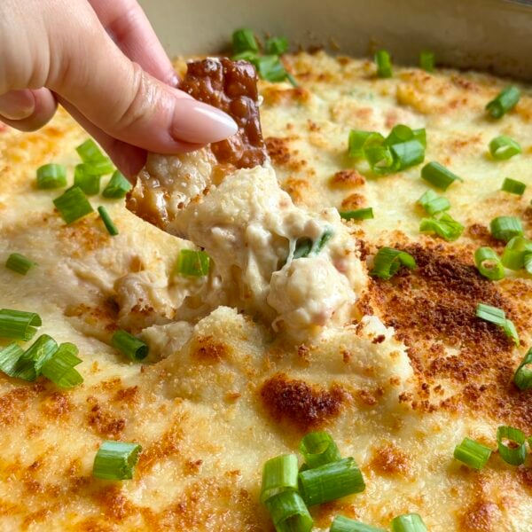 Hand dipping a crisp wonton chip into bubbling crab rangoon dip with green onions