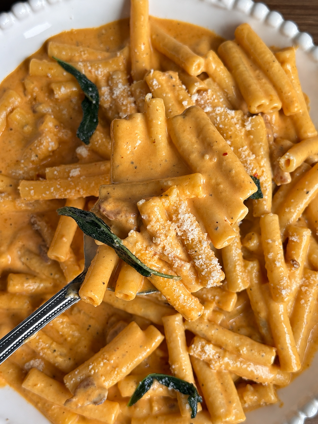 Fork lifting ziti coated in silky pumpkin vodka sauce with fried sage leaves