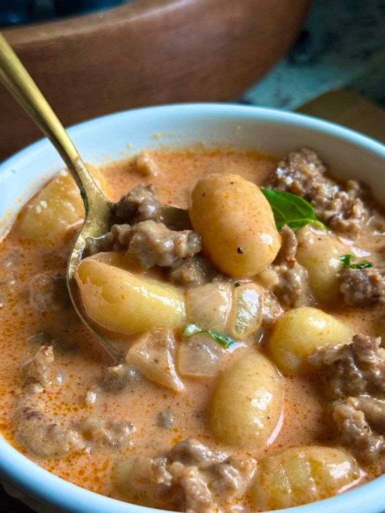 Gold spoon lifting pillowy gnocchi and sausage from creamy vodka soup