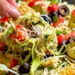 Hand lifting a loaded tortilla chip from layered taco dip with olives and jalapenos