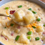 Gold spoon lifting potato chunks from loaded baked potato soup with bacon and chives