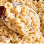 Wooden spoon lifting a heap of ring pasta coated in creamy alfredo sauce