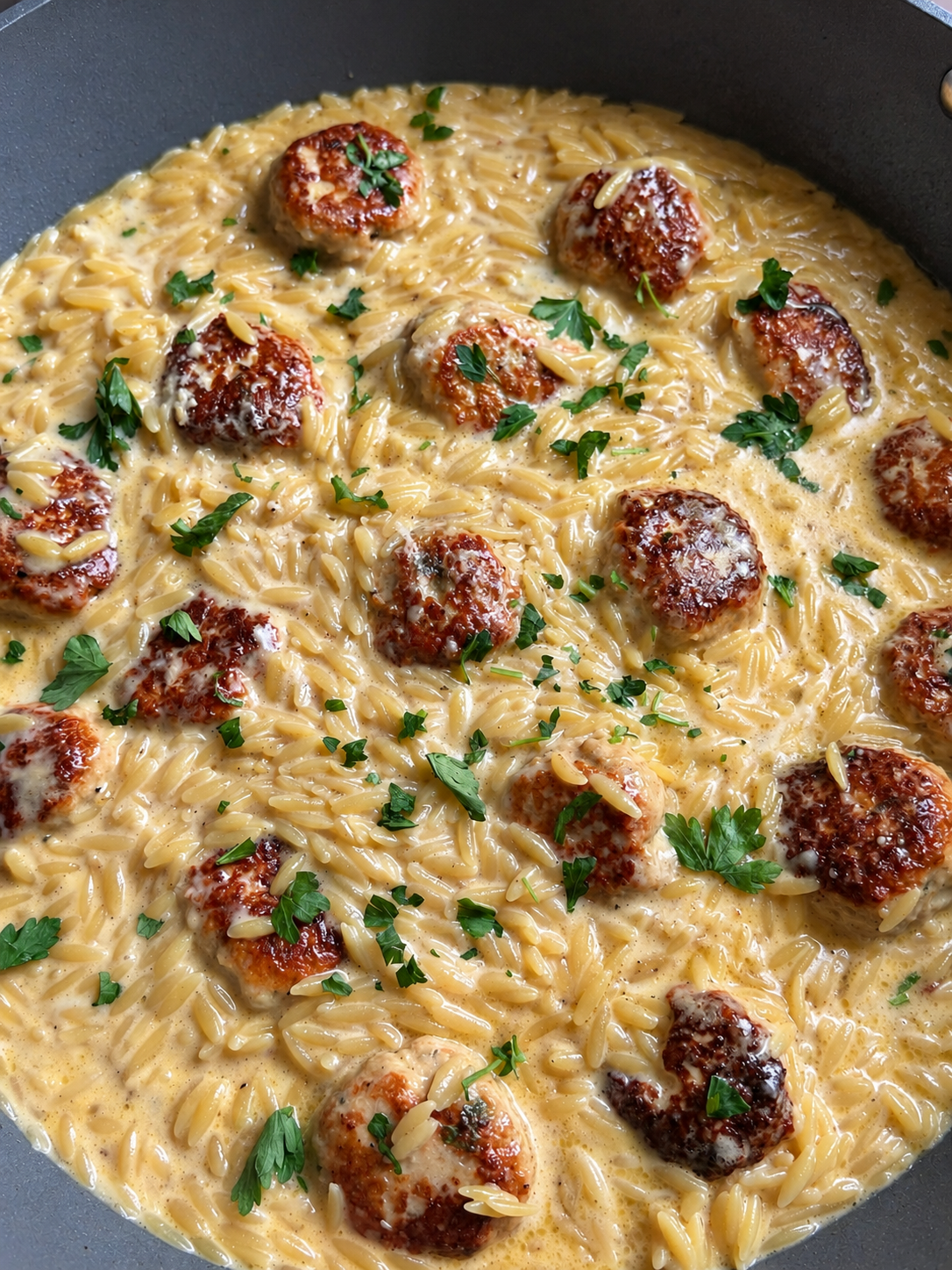 Skillet of chicken meatballs nestled in creamy orzo, flecked with fresh parsley
