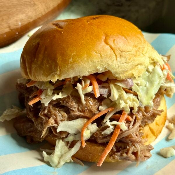 BBQ pulled pork piled on a brioche bun with crunchy coleslaw, on a striped plate