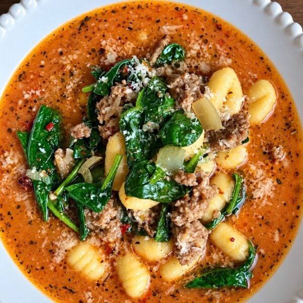Creamy sausage gnocchi soup with wilted spinach and parmesan in a white scalloped bowl