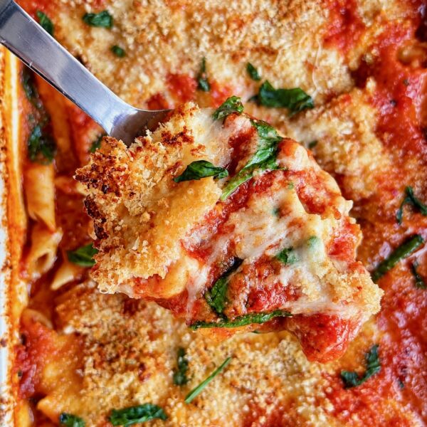 Server lifting chicken parmesan casserole with golden breadcrumb topping and basil