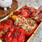 Hand spooning rice filling into roasted red peppers and tomatoes in a baking dish
