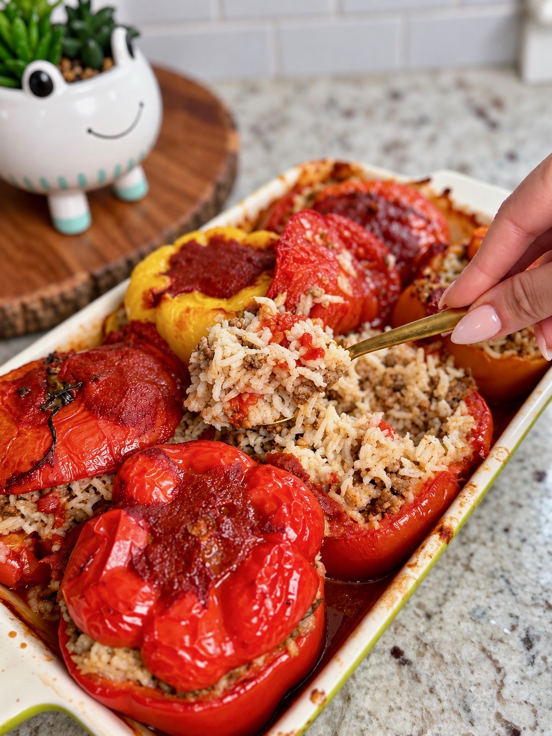 Hand spooning rice filling into roasted red peppers and tomatoes in a baking dish