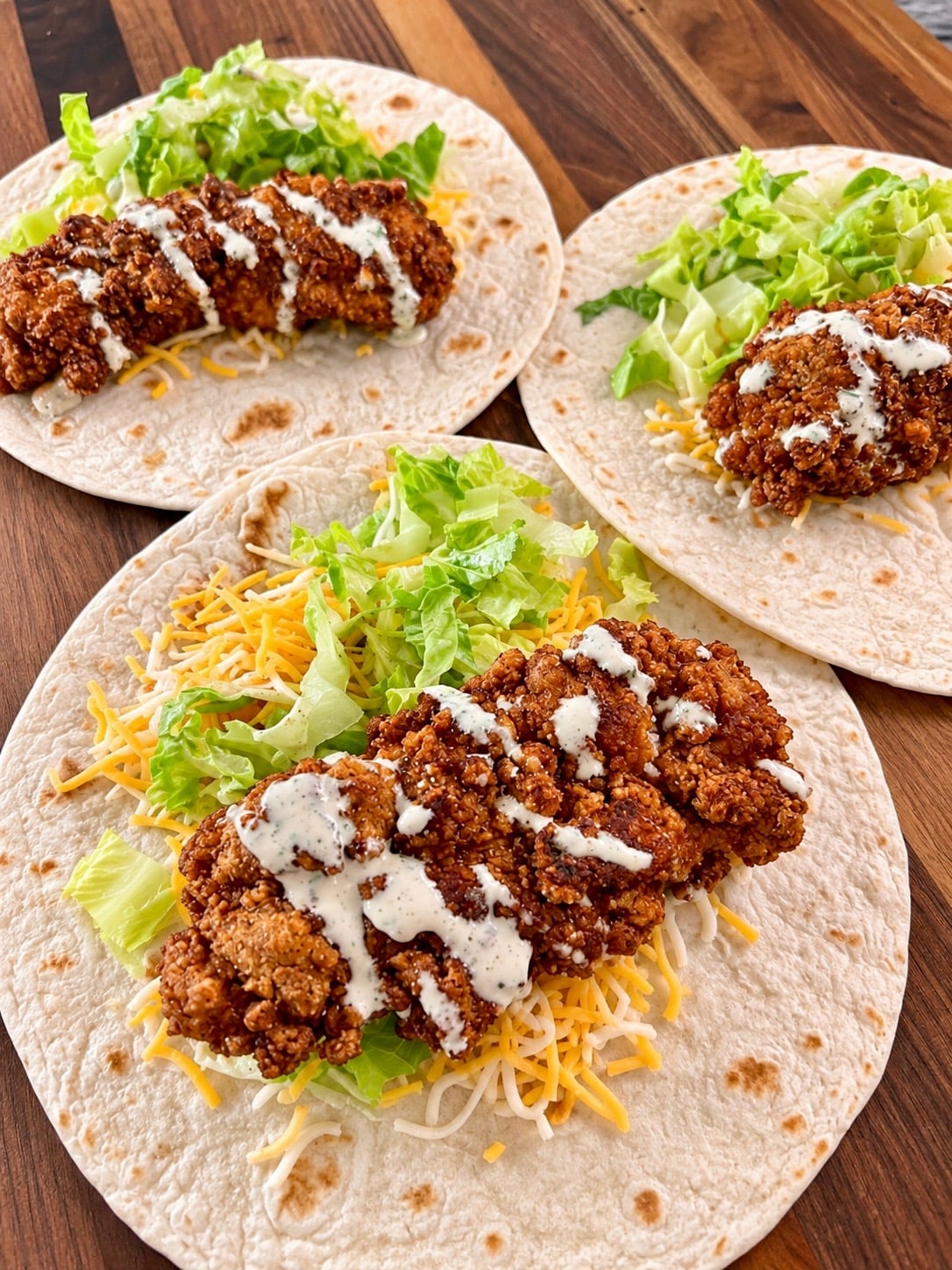 Crispy chicken snack wraps with shredded lettuce, cheddar and ranch drizzle on flour tortillas