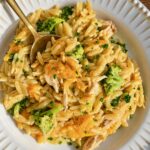 Gold spoon in a white bowl of cheesy chicken broccoli orzo casserole