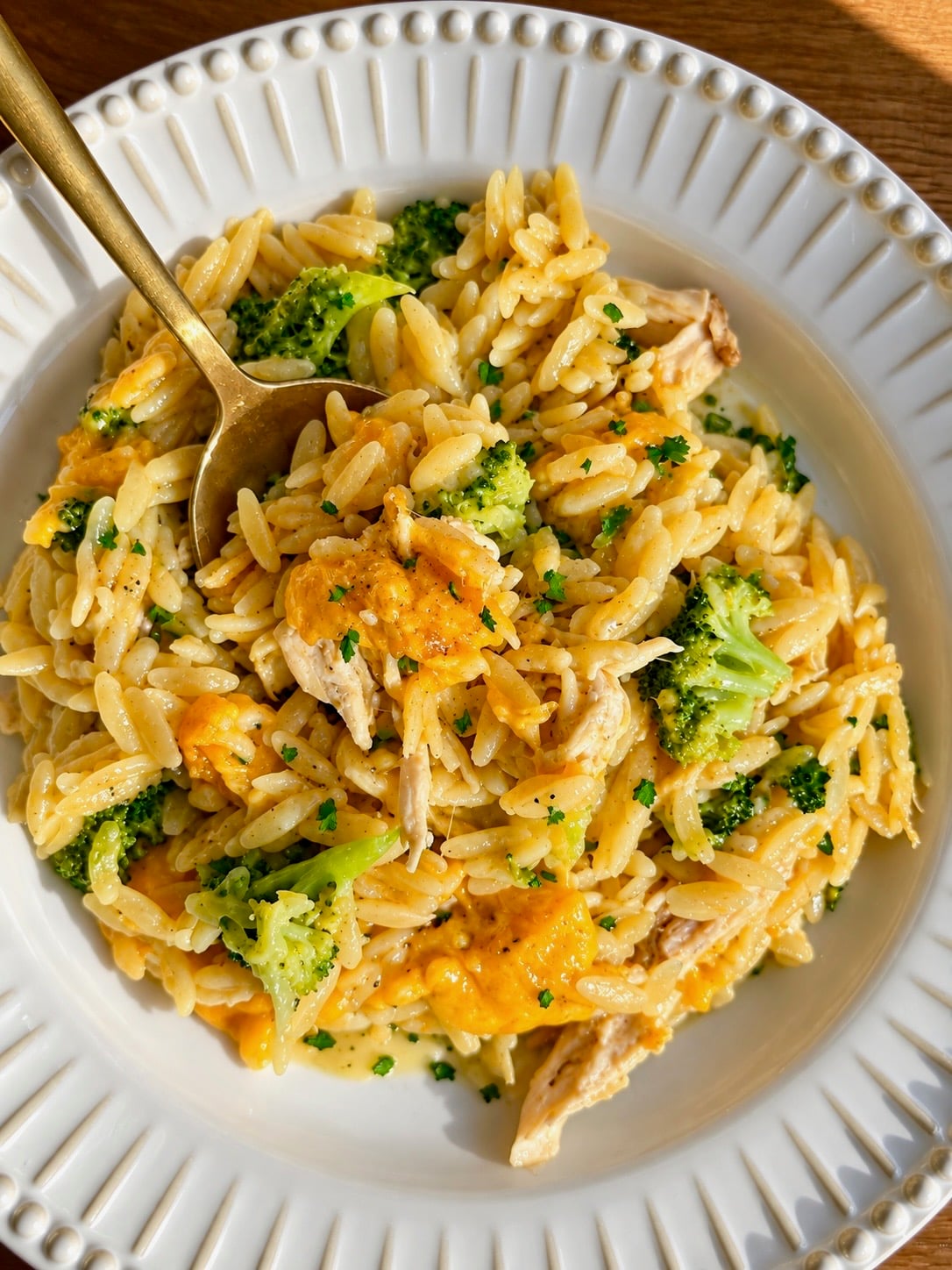 Gold spoon in a white bowl of cheesy chicken broccoli orzo casserole