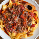 Osso buco ragu over wide ribbon pasta with carrots, a marrow bone and grated Parmesan