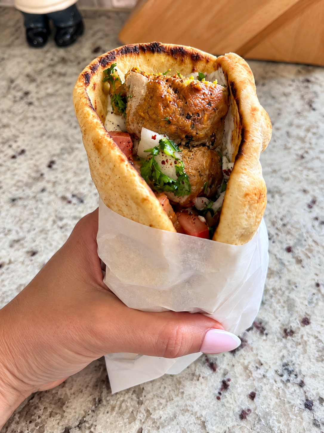 Hand holding a warm pita stuffed with turkey kebab and chopped sumac salad