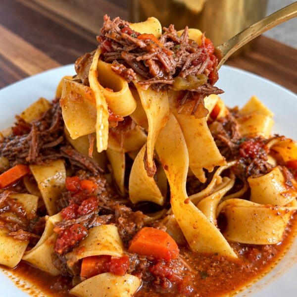 Fork lifting pappardelle tossed with shredded braised short rib and carrots in red sauce