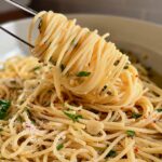 Fork twirling spaghetti aglio e olio flecked with parsley and red pepper flakes