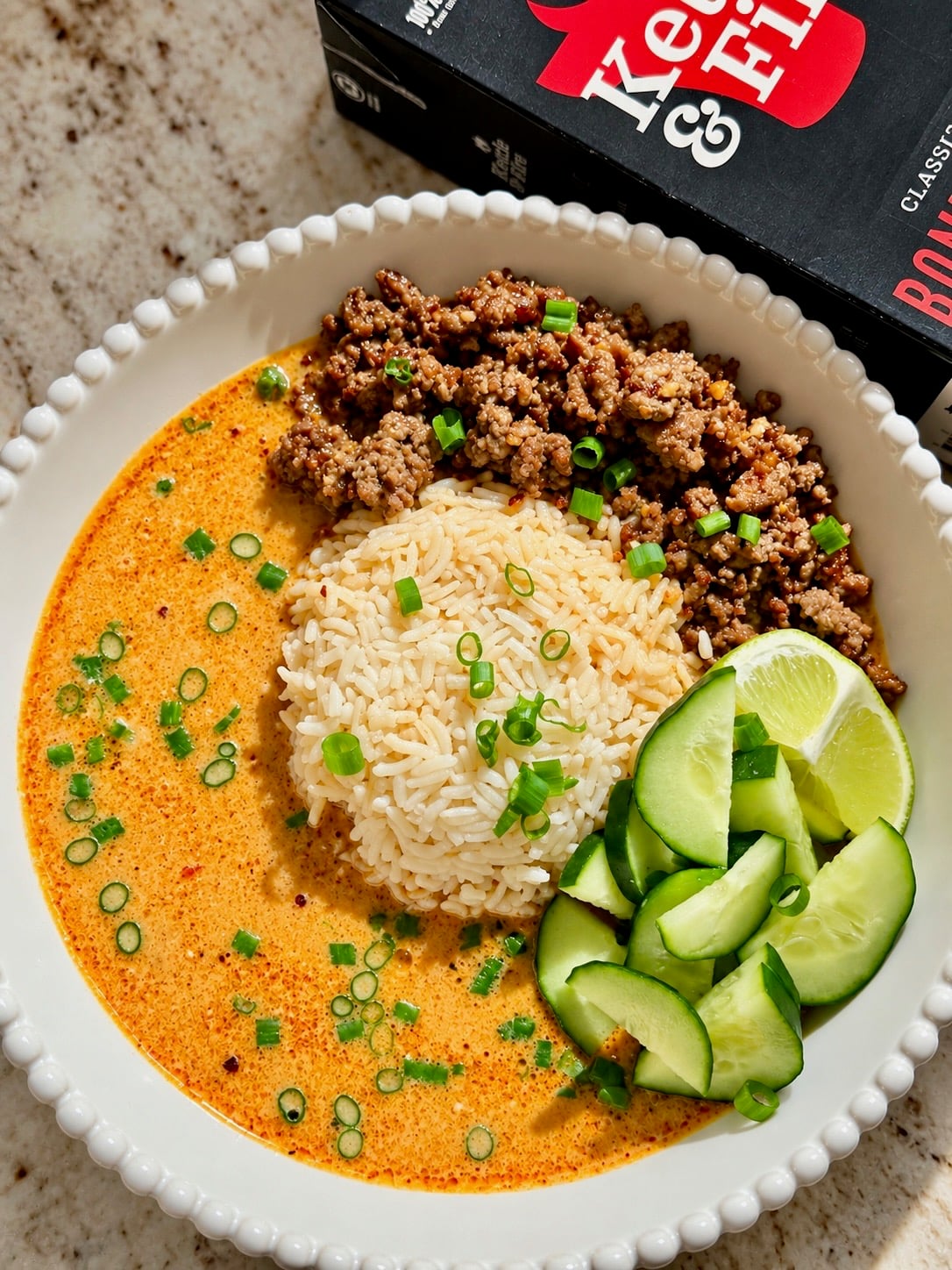 Coconut broth bowl with ground beef, jasmine rice, cucumber and lime wedges